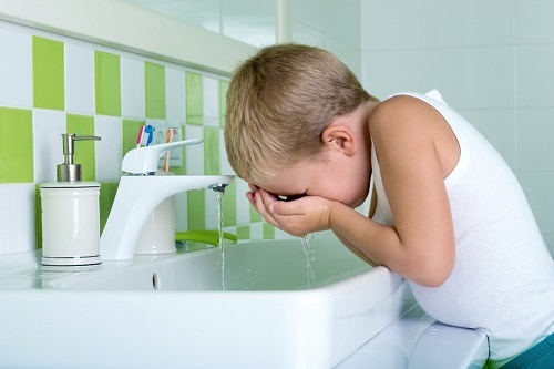 Child putting water on his face with his hands at a bathroom sink