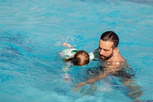 Man teaching a child to swim in a horizontal position with her face in the water